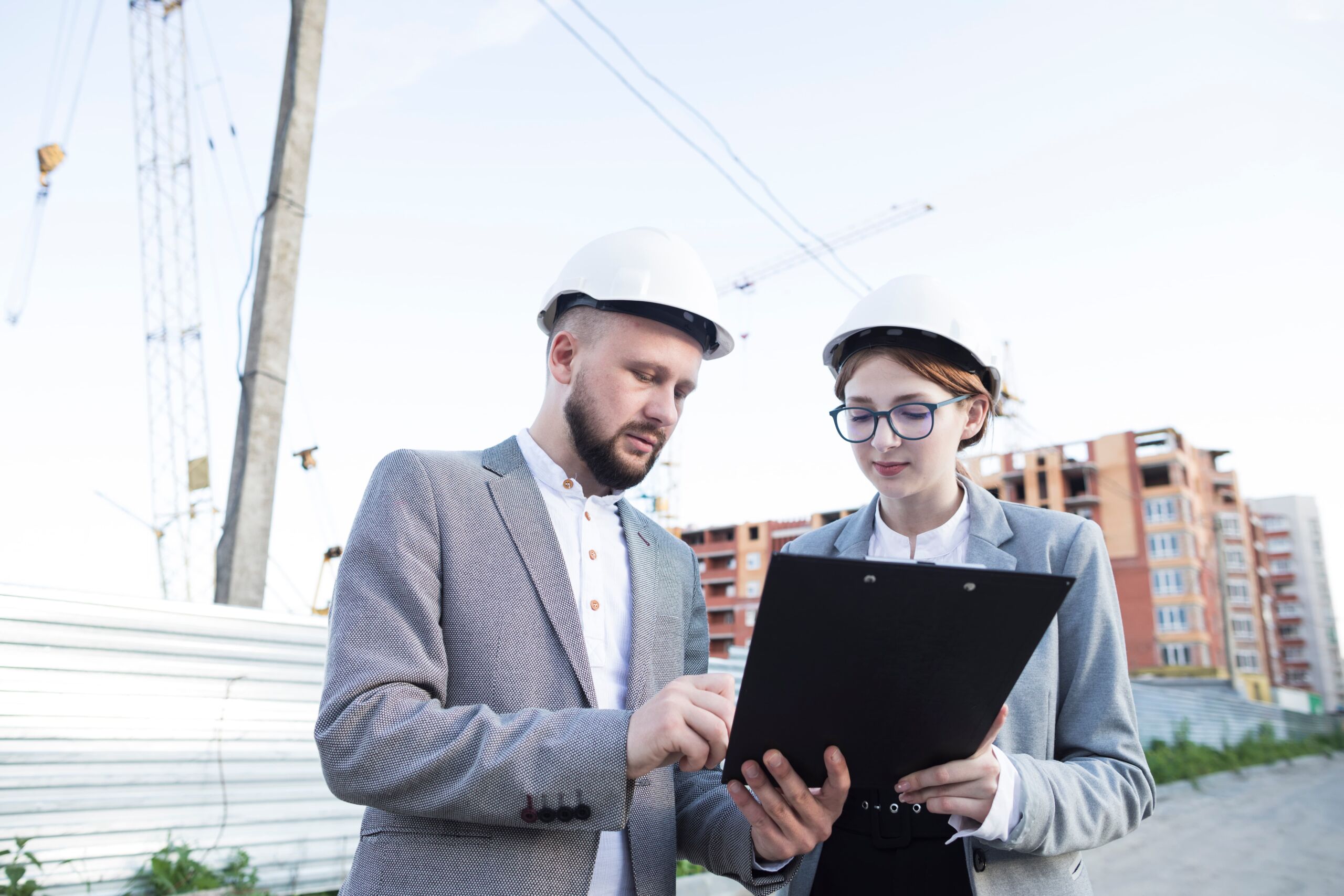 young-female-male-architect-wearing-hard-hat-looking-clipboard (1) (1)